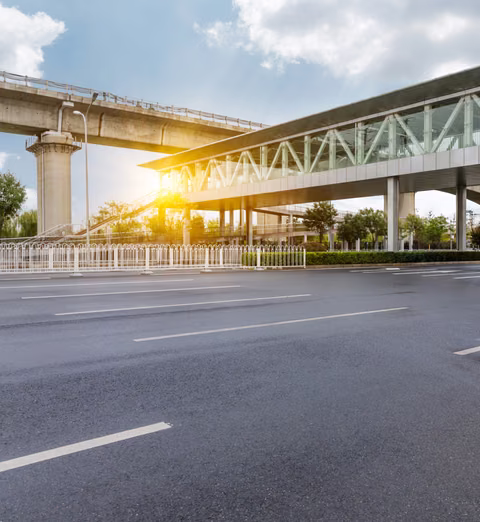 Elevated rail viaduct and station beside an empty highway at sunrise